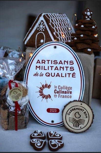 Une plaque portant le logo Artisans Militants de la Qualité au milieu de friandises de Noël